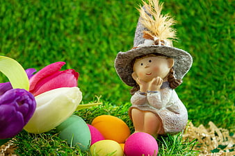 Easter figurine with colorful eggs and tulips on green grass