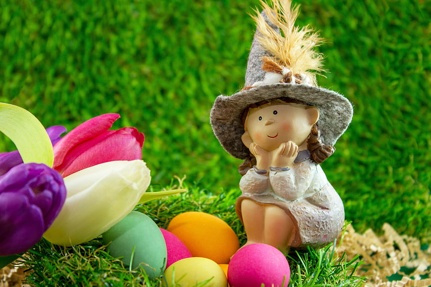 Easter figurine with colorful eggs and tulips on green grass