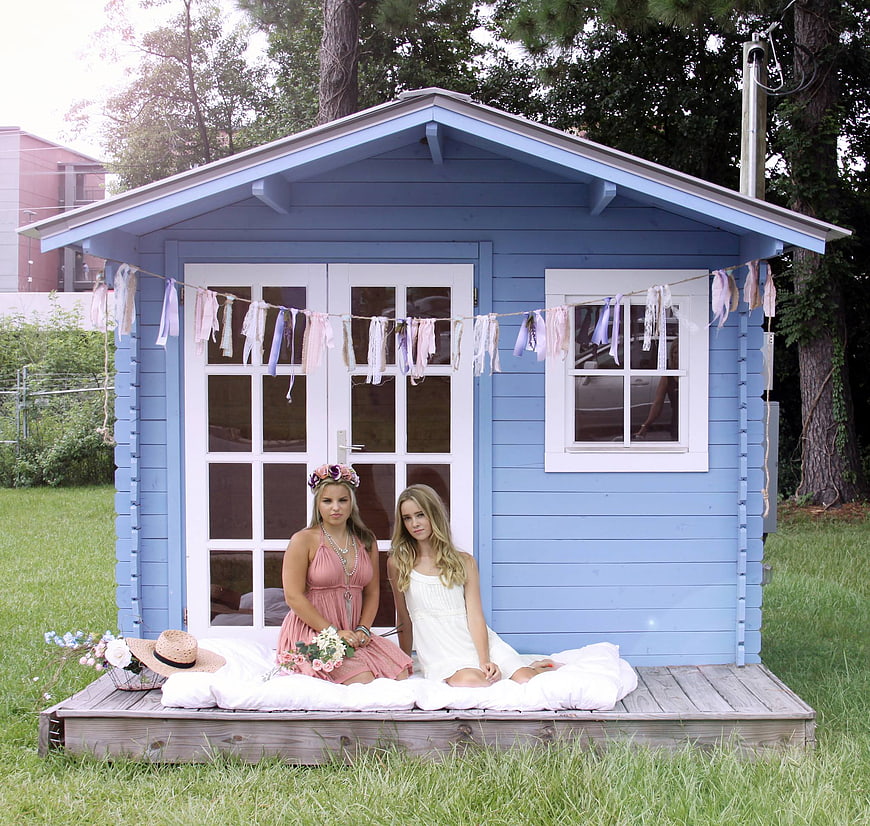 Two young women sitting on a blue garden shed porch