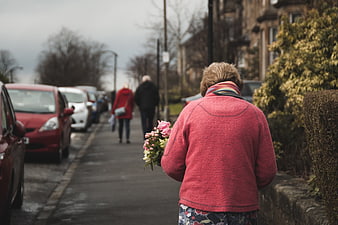 Senior woman walking down street carrying pink flowers