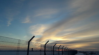 Security fence silhouette against dramatic sunset sky