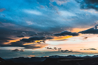 Dramatic sunset over mountain range with blue and orange clouds