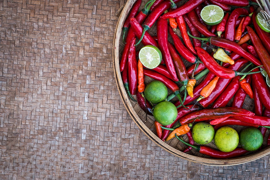 Top view of red chili peppers and limes in a woven basket