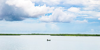 Small boat on calm river with dramatic clouds and green mangroves