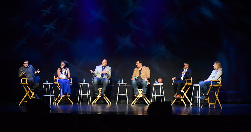 Panel Discussion With Six Speakers On A Dark Stage