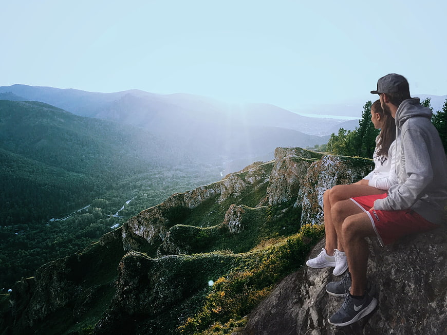 Couple sitting on cliff edge overlooking mountain valley