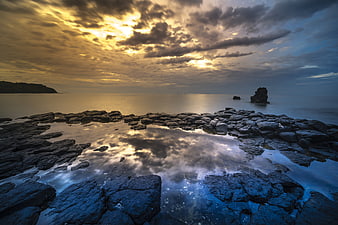 Dramatic sunset over rocky volcanic coastline with tidal pool reflection
