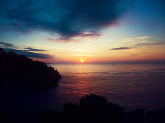 Dramatic Sunset Over Ocean with Silhouetted Coastline