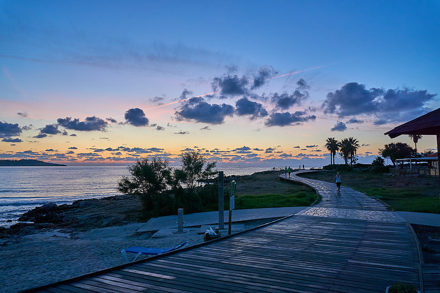Wooden boardwalk path along beach at sunrise with runner