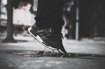 Close-up of black sneaker splashing in urban puddle