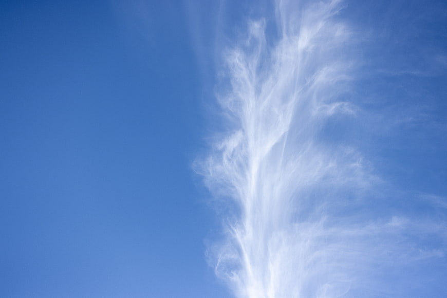 Wispy white clouds against a clear blue sky background