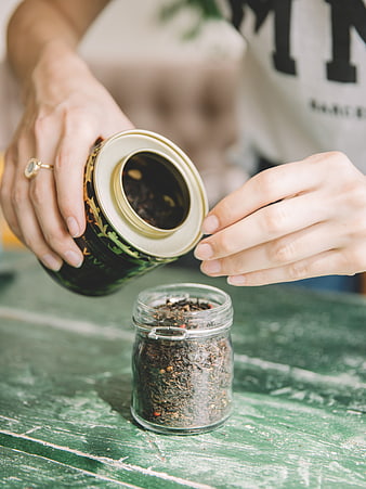 Hands pouring loose leaf tea into glass jar on rustic table