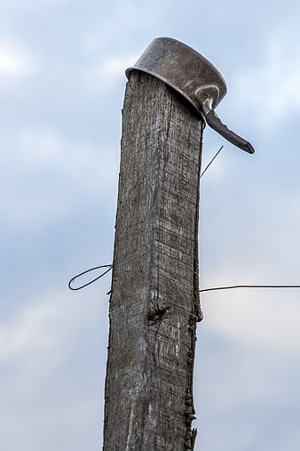 Old metal pot on weathered wooden post against cloudy sky