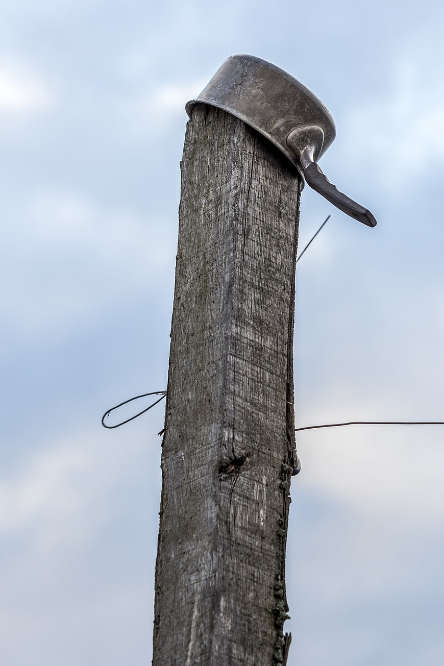 Old metal pot on weathered wooden post against cloudy sky