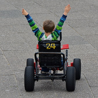 Boy in go-kart with arms raised in victory on paved surface