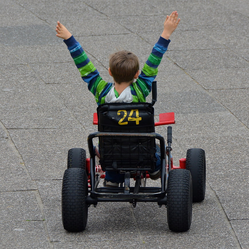 Boy in go-kart with arms raised in victory on paved surface