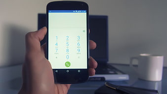 Hand holding smartphone with dial pad in office workspace