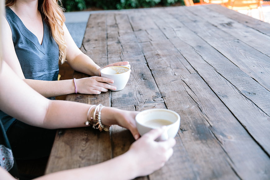 Two women holding coffee cups at rustic wooden table