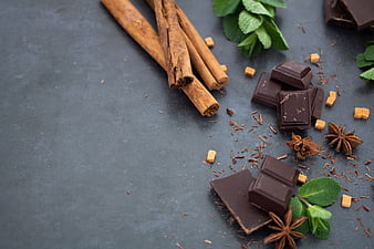 Dark chocolate pieces, cinnamon sticks, and mint leaves on a slate surface