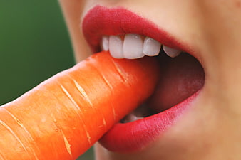 Close-up of woman eating raw carrot with red lipstick