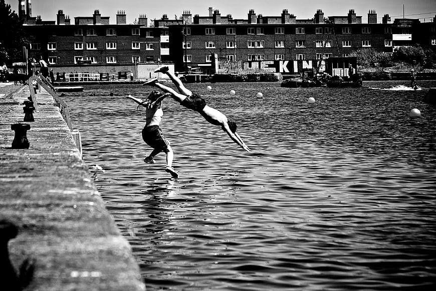 Two people jumping into river from concrete pier