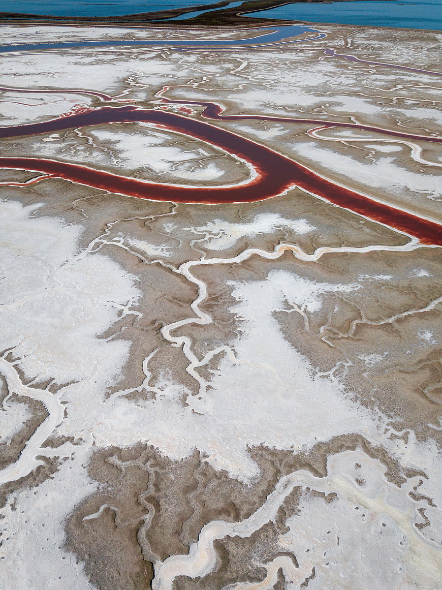 Aerial view of red river winding through white salt flats
