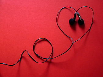 Black earphones arranged in heart shape on red background