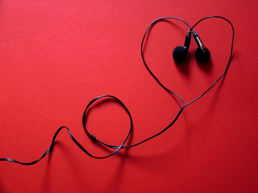 Black earphones arranged in heart shape on red background