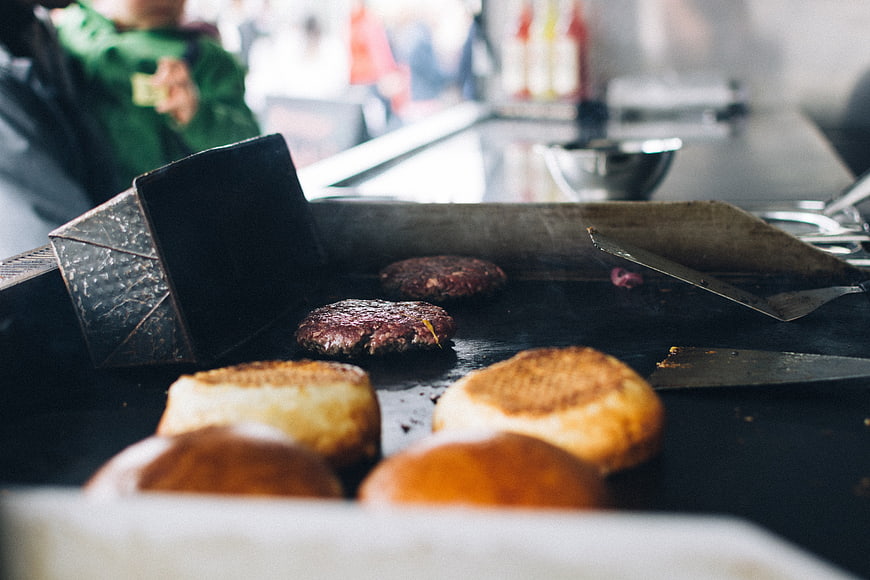 Beef burgers and buns grilling on a flat top grill