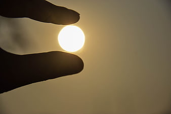 Hand Silhouette Pinching Sun Against Golden Sky