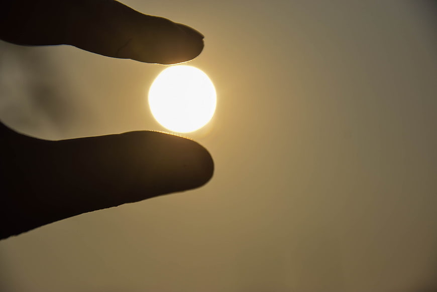 Hand Silhouette Pinching Sun Against Golden Sky