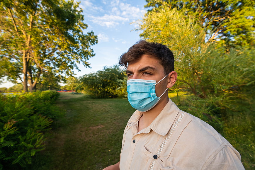 Young man wearing blue medical mask in park