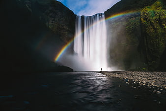 Lone Figure Standing Before Massive Waterfall with Rainbow