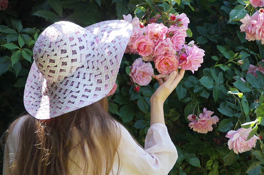 Woman in Crochet Hat Smelling Pink Roses in Garden