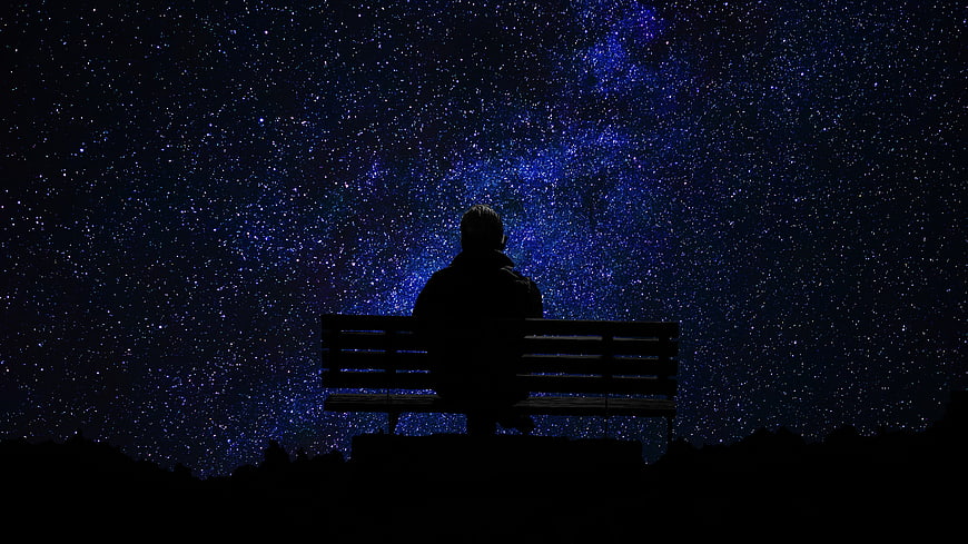 Silhouette of Man Sitting on Bench Under Starry Night Sky