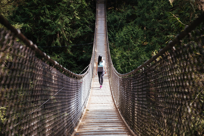Woman Walking on Suspension Bridge in Forest
