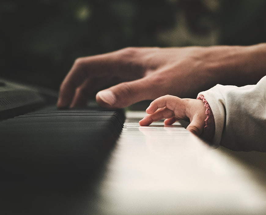 Adult and baby hands playing piano keys together