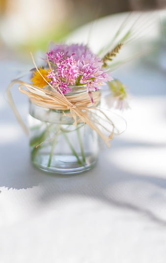 Small glass jar with wildflowers and raffia ribbon on white table