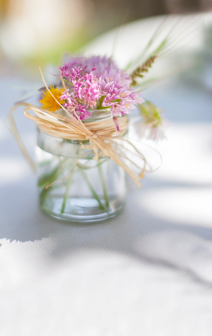 Small glass jar with wildflowers and raffia ribbon on white table