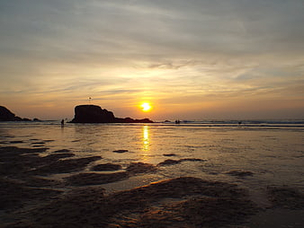 Golden Sunset Over Rocky Beach with Silhouetted Figures