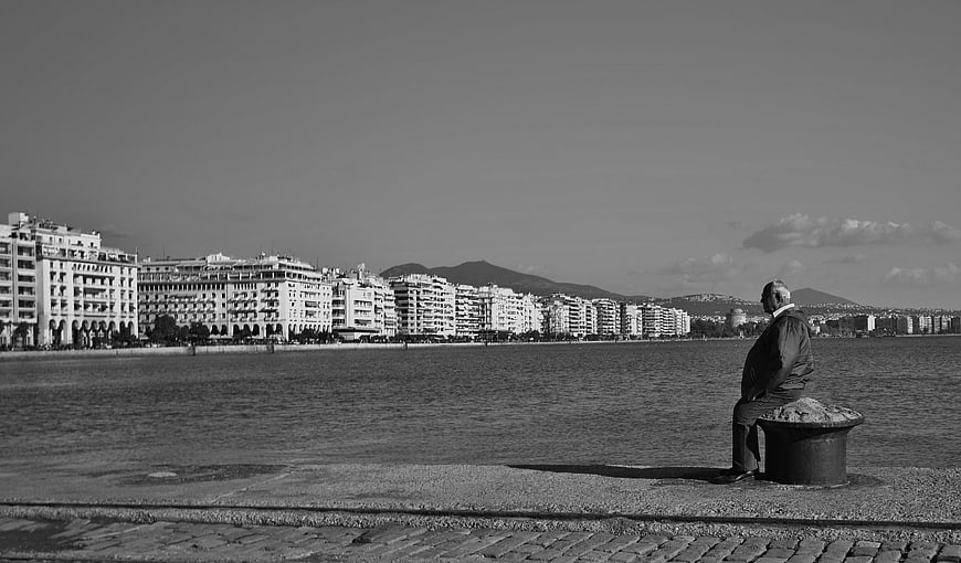 Senior man sitting alone on seaside promenade in black and white