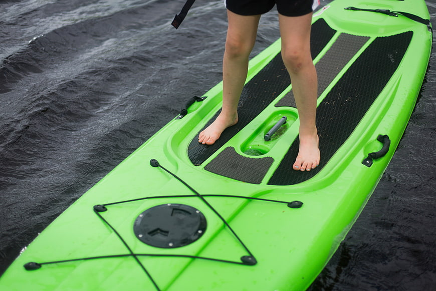 Close-up of bare feet standing on a green paddleboard