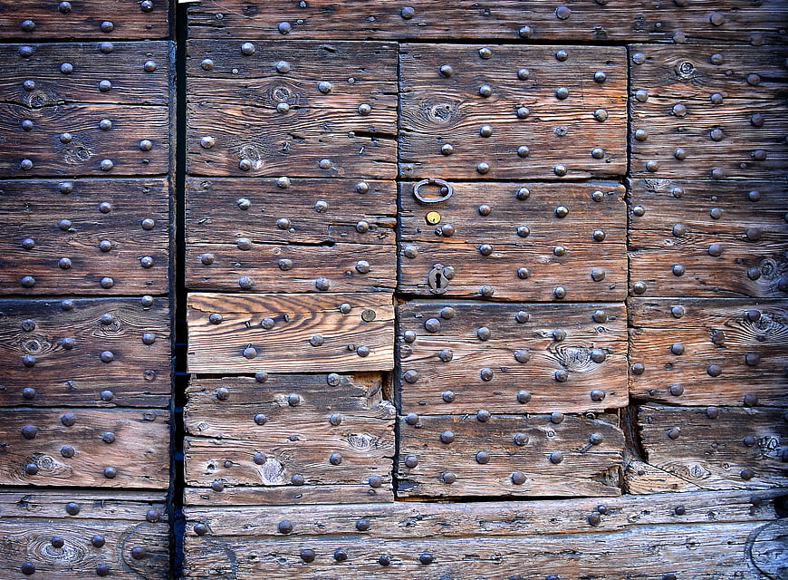 Close-up of weathered wooden door with metal studs and lock
