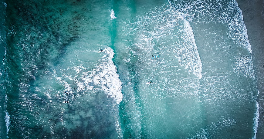 Aerial View of Surfers Riding Turquoise Ocean Waves