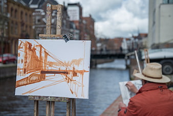 Artist painting bridge on easel by canal