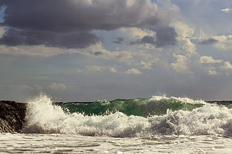 Powerful Green Wave Crashing on Rocky Coast Under Cloudy Sky