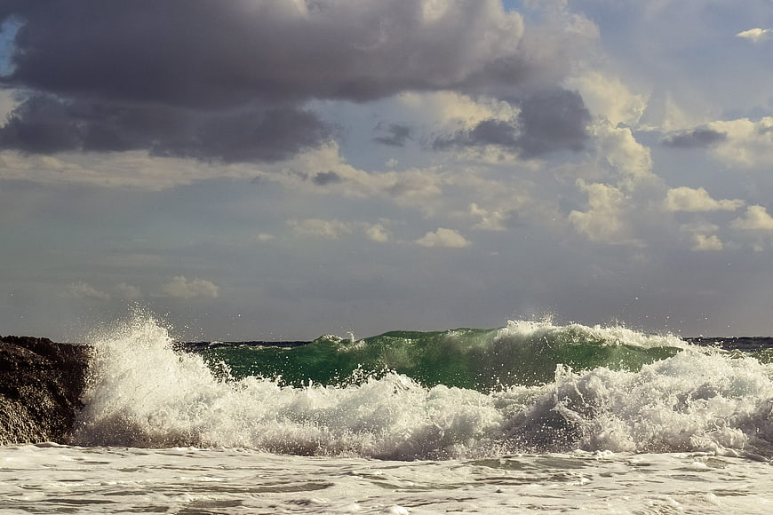 Powerful Green Wave Crashing on Rocky Coast Under Cloudy Sky