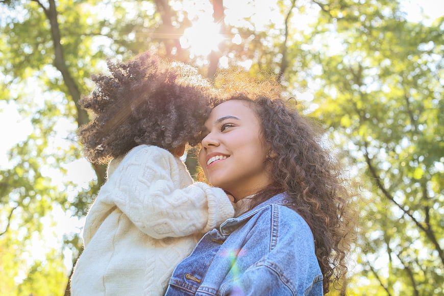 Happy mother hugging daughter in sunny park