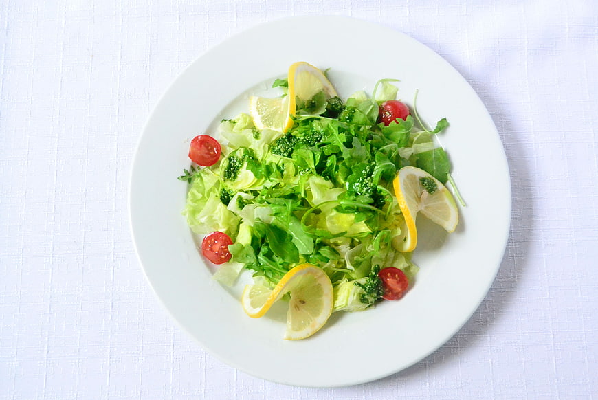 Fresh Green Salad with Lemon and Tomatoes on White Plate