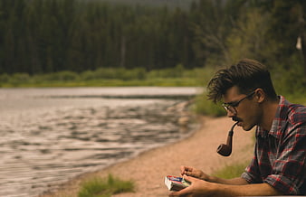 Man smoking pipe by river in nature